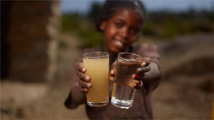 A child holding two glasses, one with dirty water and one with clean water