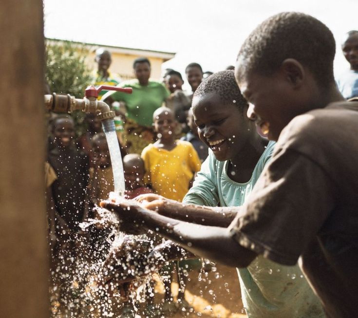 Multiple hands sharing water from a communal pipe showing collective dependence on scarce water sources